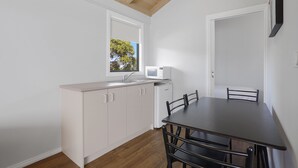 Cocina compacta con comedor, vigas de madera en el techo y ventana con vistas a árboles.