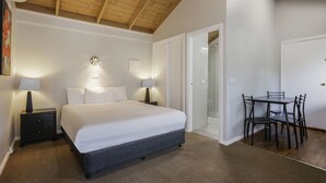 Un dormitorio con cama, lámparas de noche, techo de madera y una zona de comedor con sillas y mesa.