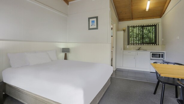 Un dormitorio con cama, escritorio, silla, una kitchenette pequeña y una ventana con persianas.