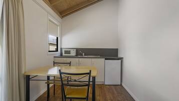 A compact kitchen with a wooden table, two chairs, a microwave, and a small refrigerator.