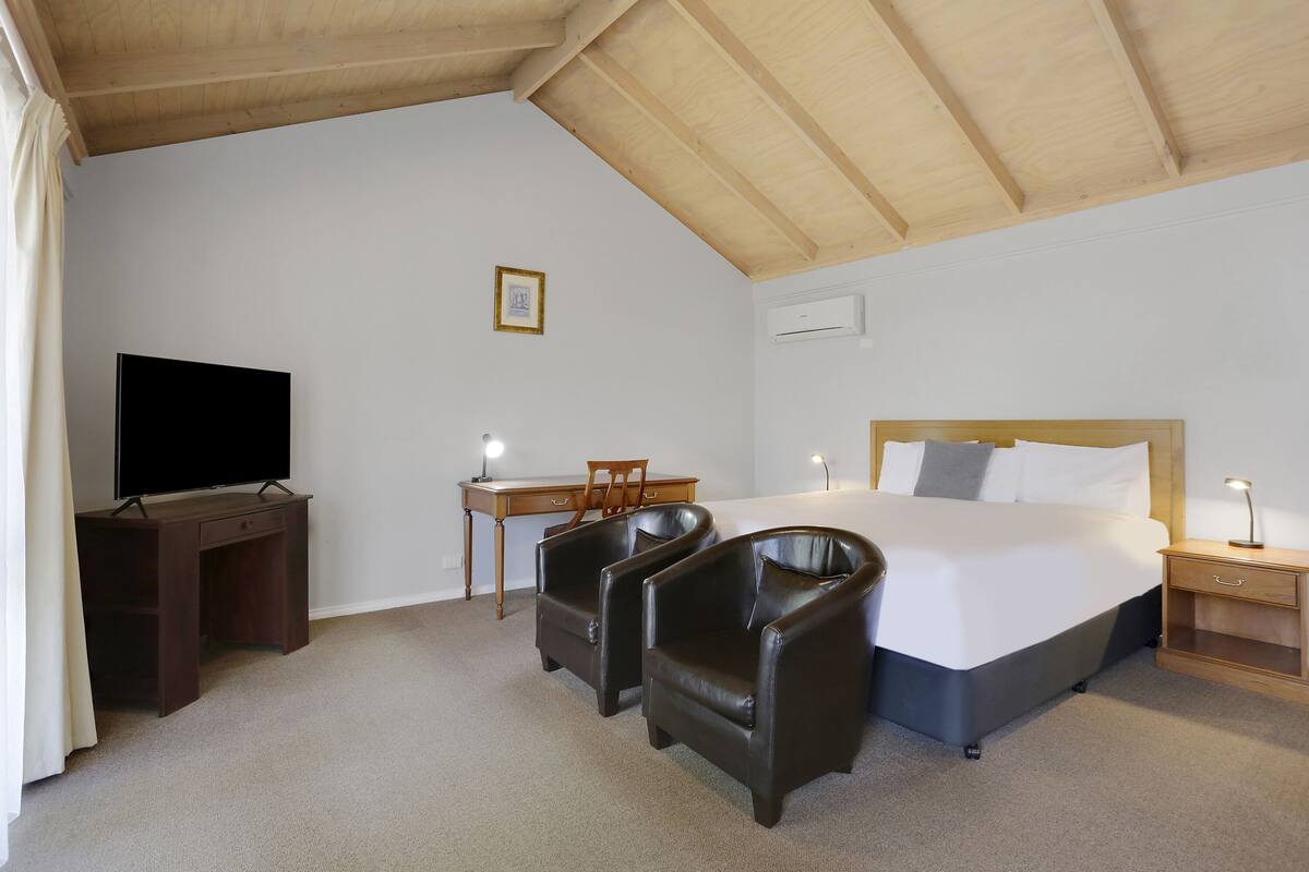 Ein Hotelzimmer mit einem Bett, zwei Ledersesseln, einem Schreibtisch mit Stuhl, einem Fernseher und einem Nachttisch mit Lampe.