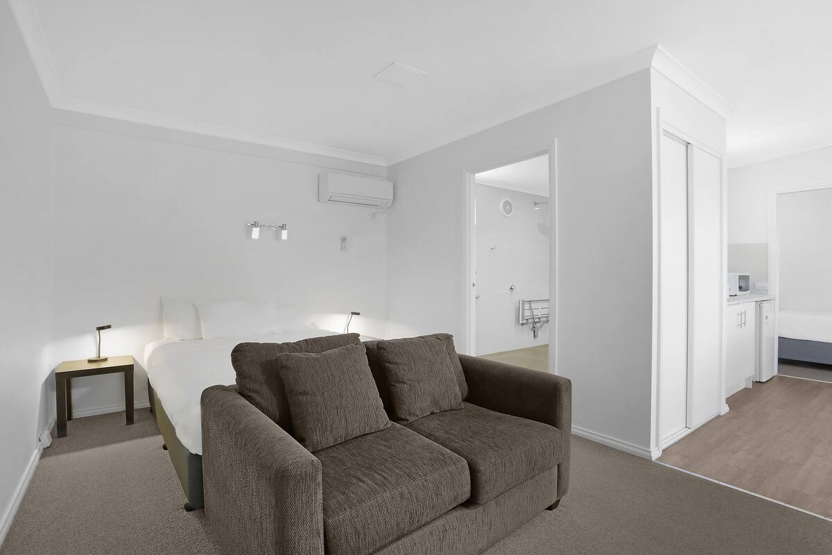 Ein modernes Hotelzimmer mit einem großen Bett, einer Couch, einem Nachttisch und einem durch eine offene Tür einsehbaren Badezimmer.