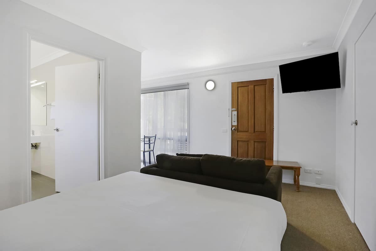 Ein Schlafzimmer mit einem großen Bett, einem an der Wand befestigten Fernseher, einer Holztür und einem kleinen Tisch.