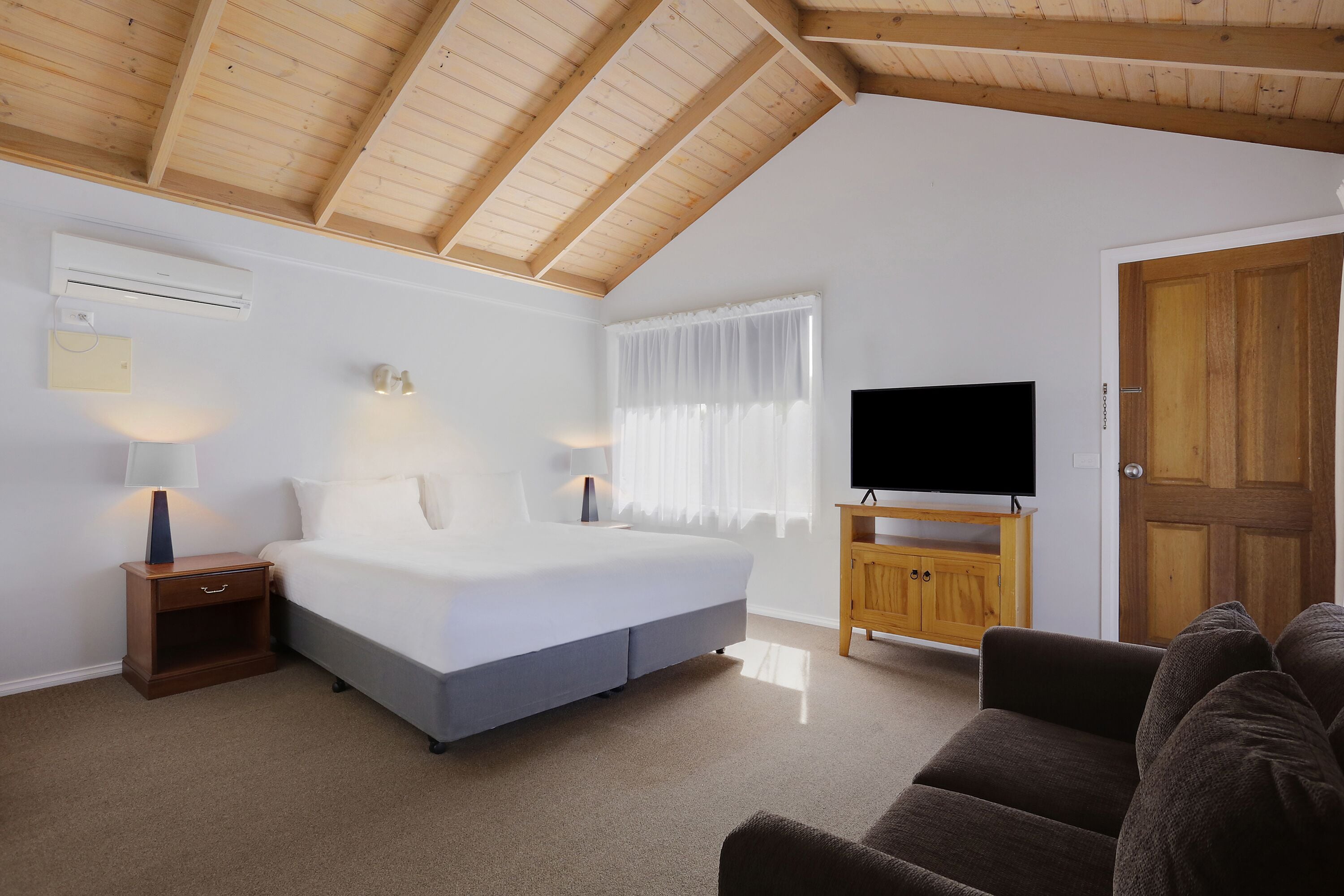 Une chambre à coucher avec un lit, des tables de chevet, un téléviseur et une porte en bois.