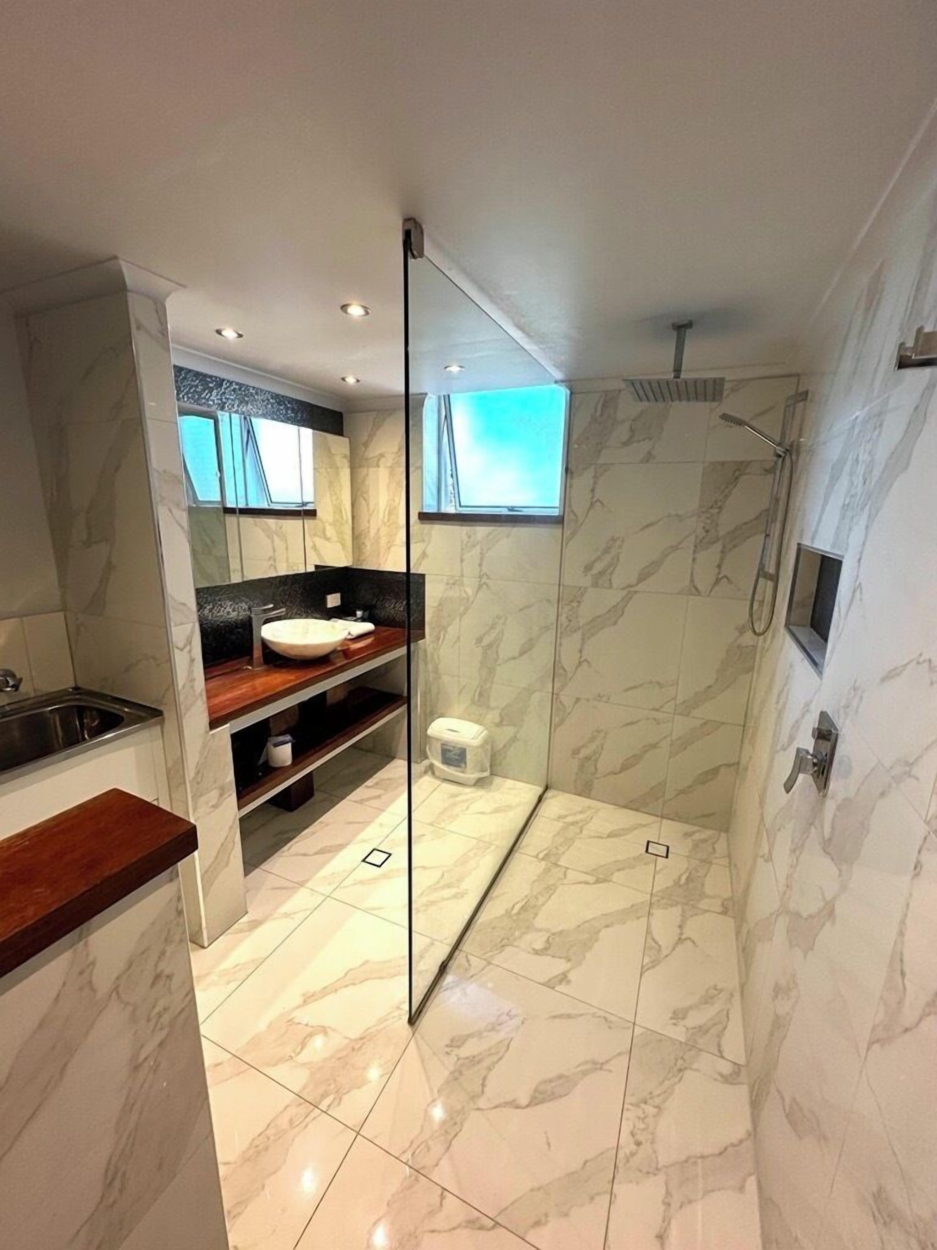 Ein modernes Badezimmer mit Marmorboden, einem Holzkosmetikschrank, einer Glasdusche und einem großen Spiegel.