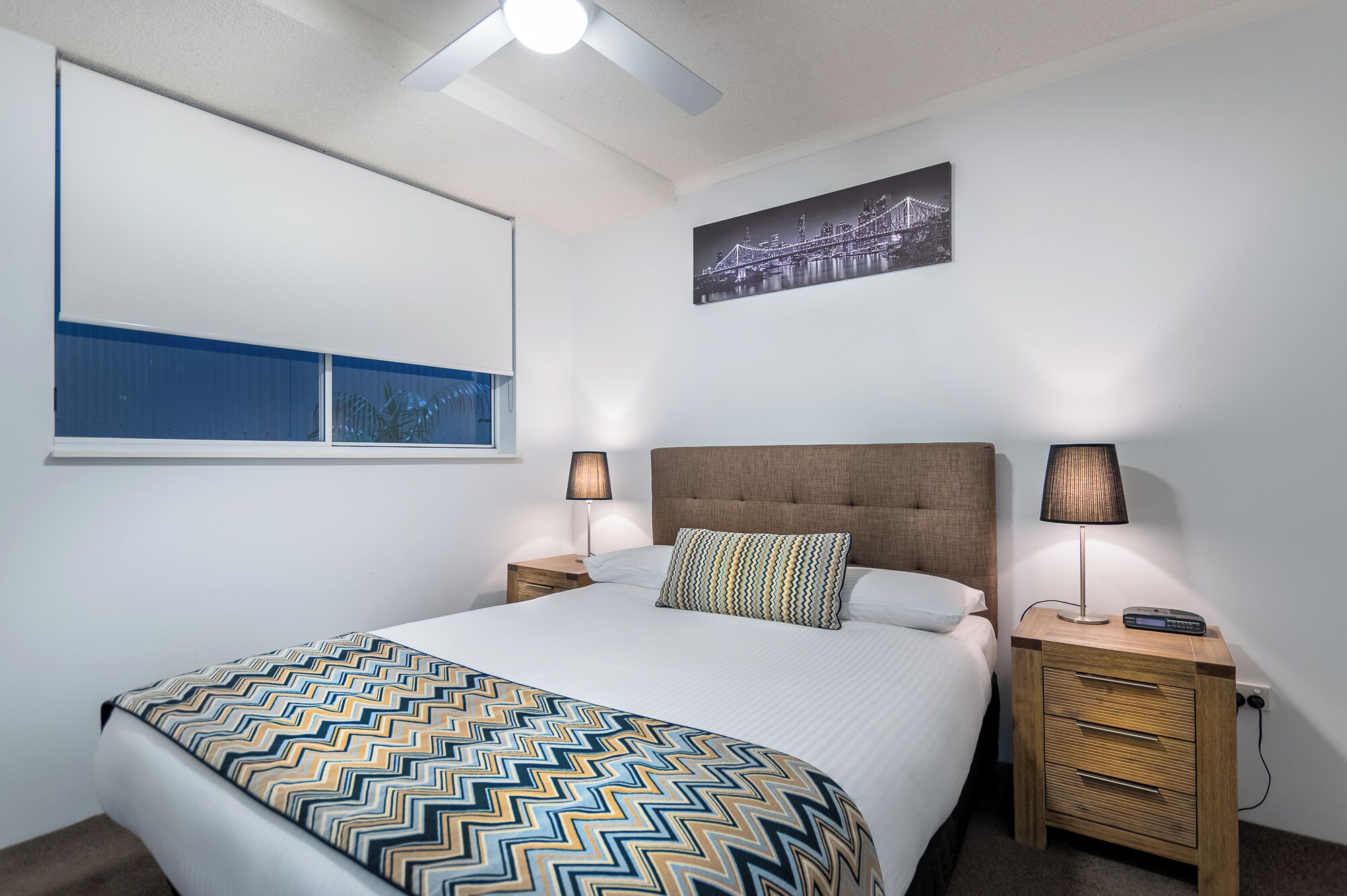 Habitació d'hotel ben ordenada amb un llit, dues taules de nit amb làmpades, un quadre penjat a la paret i una finestra amb vistes.