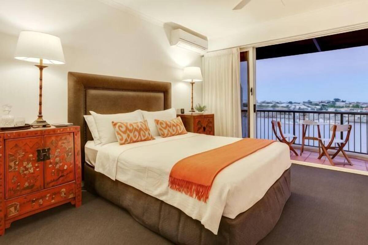 Une chambre d’hôtel avec un grand lit, deux tables de chevet, un balcon donnant sur l’eau et un fauteuil.
