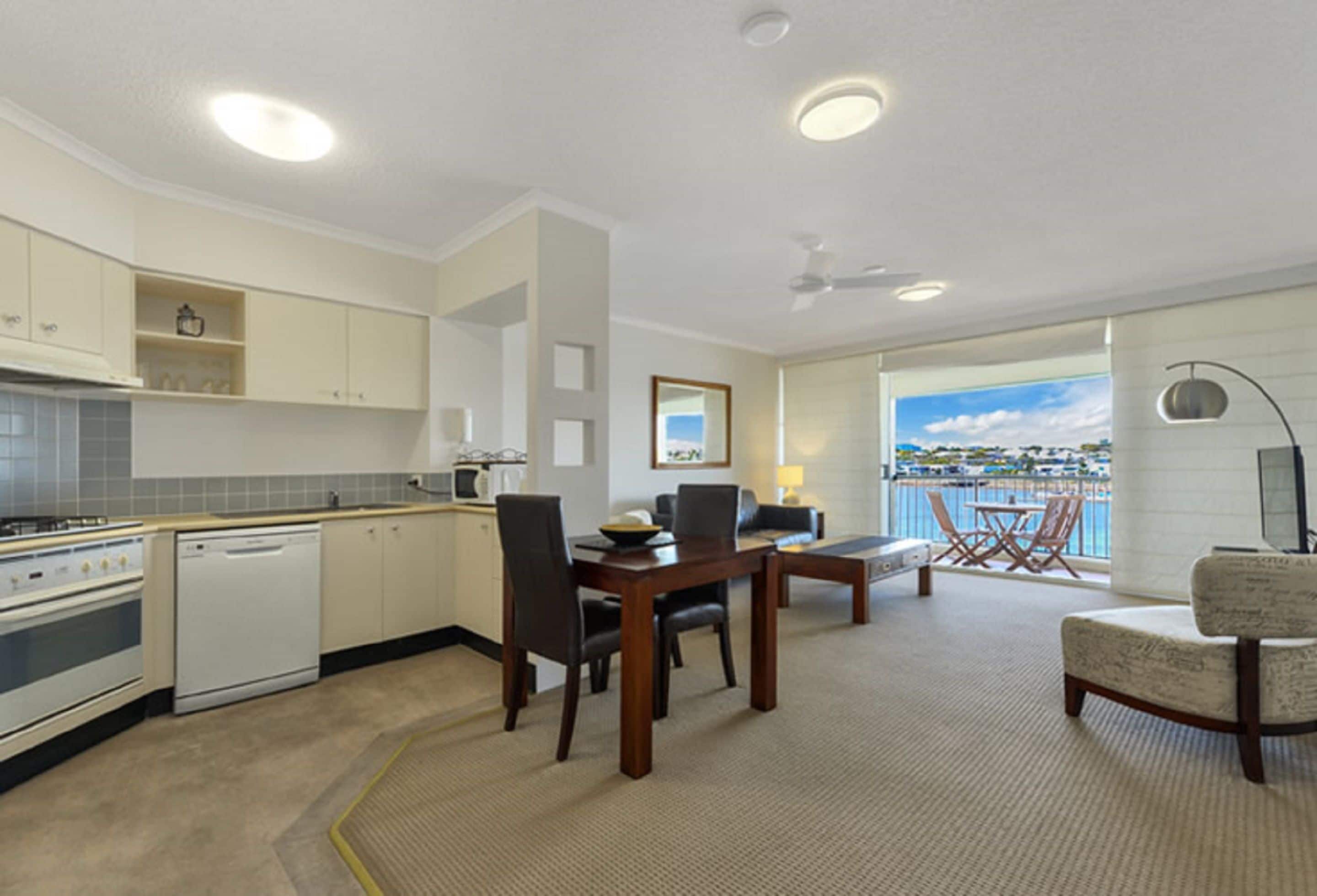 Eine moderne Küche mit weißen Schränken, ein Essbereich mit einem Holztisch und Stühlen sowie ein Balkon mit Blick aufs Meer.
