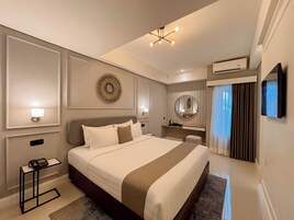 Una habitación de hotel moderna con una cama grande, mesitas de noche, un espejo, un televisor y un aire acondicionado.