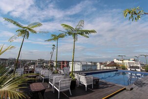 Un área de piscina en la azotea con sillas de mimbre blanco, una piscina y palmeras.