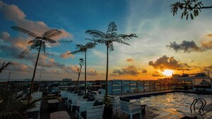 A rooftop pool area with lounge chairs and palm trees, overlooking a cityscape at sunset. - Hotel FortunaGrande Malioboro (formerly Hotel Dafam Fortuna) (Yogyakarta)