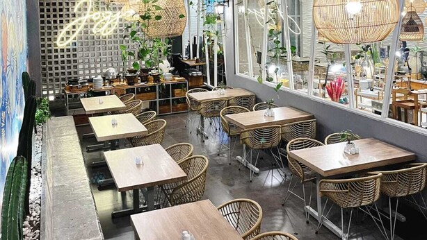 A restaurant with wicker tables and chairs, hanging rattan lamps, and a mural on the wall. - Hotel FortunaGrande Malioboro (formerly Hotel Dafam Fortuna) (Yogyakarta)