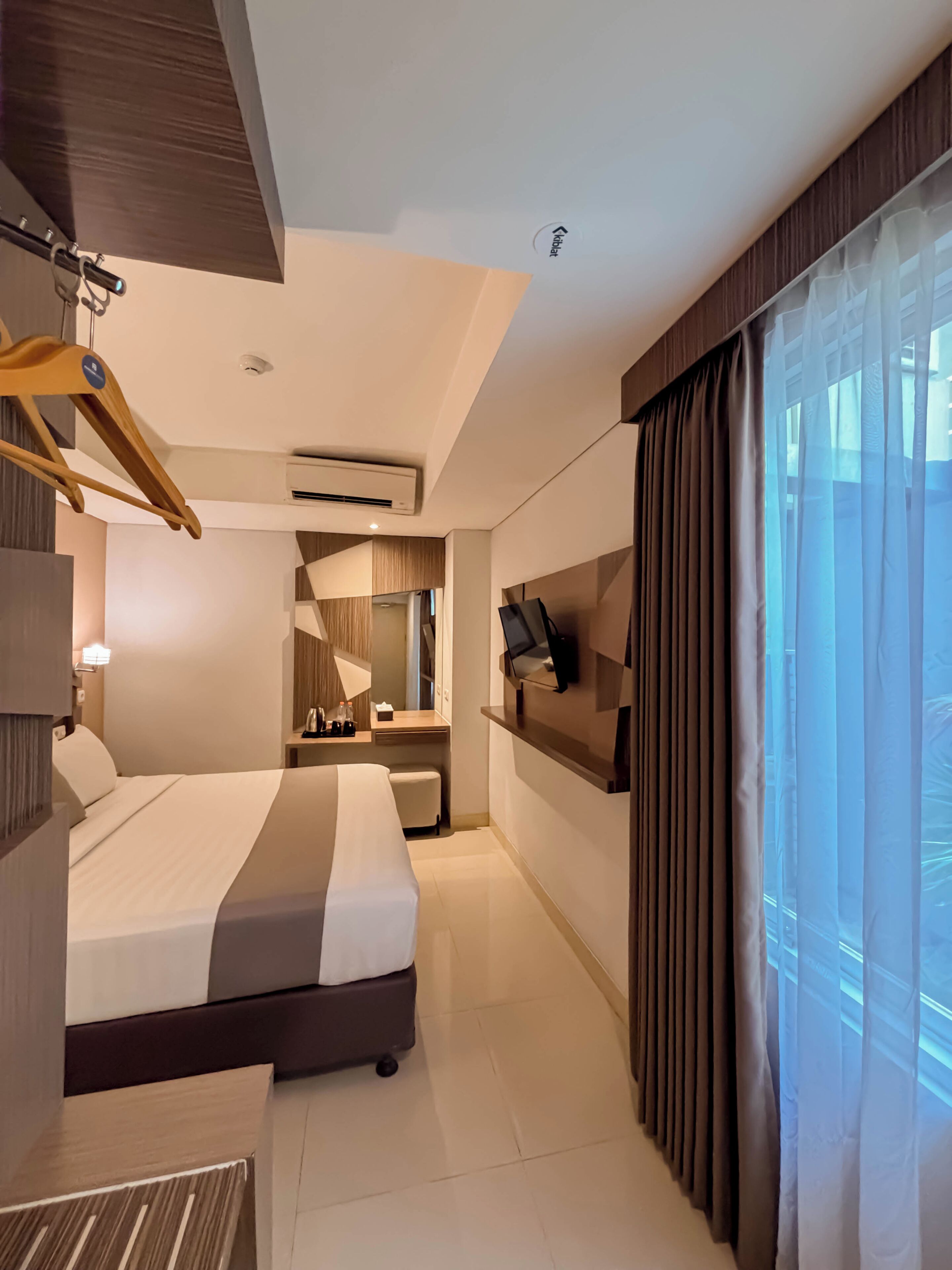 Ein modernes Hotelzimmer mit Bett, Schreibtisch, Fernseher und großen Fenstern.