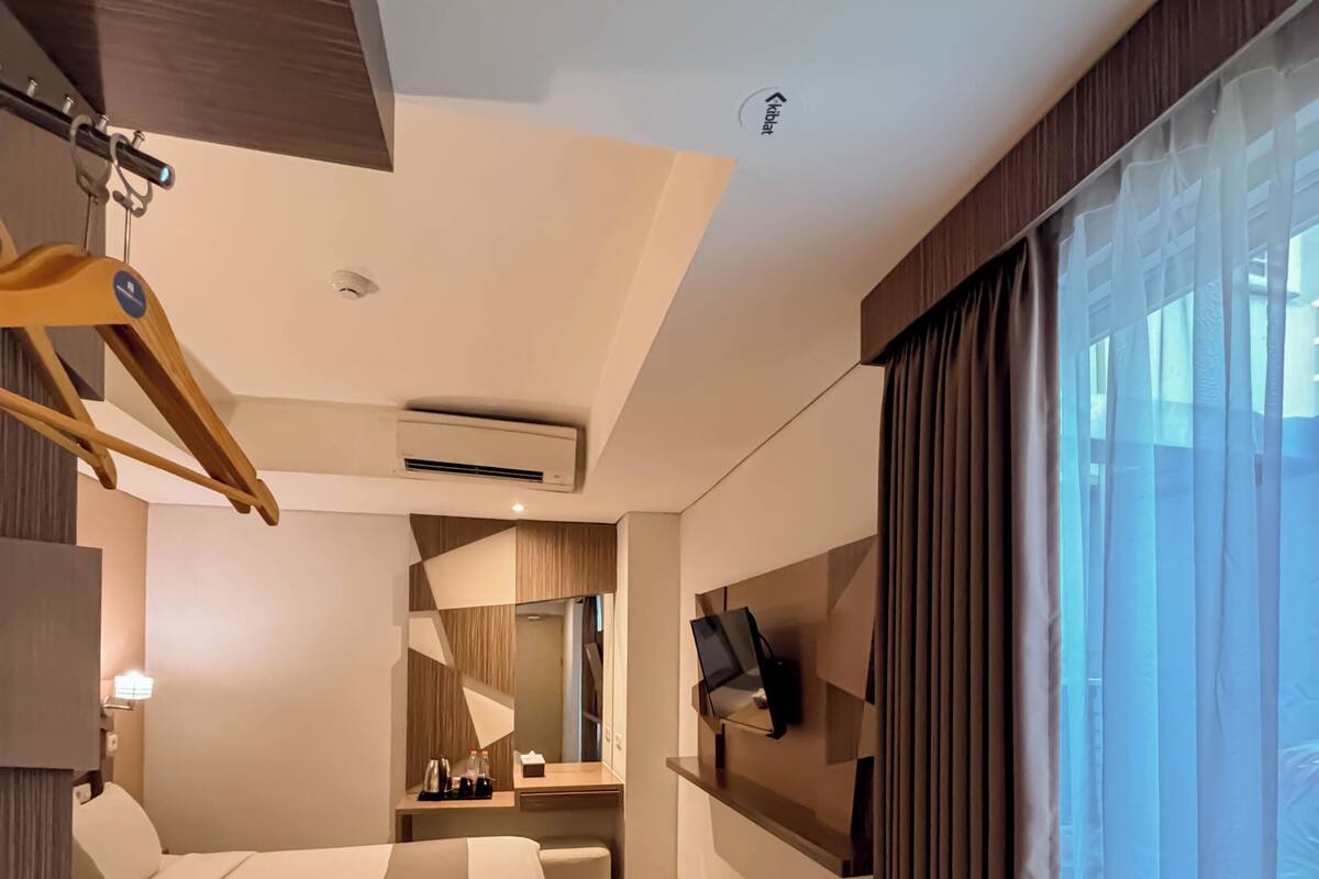 A modern hotel room with a bed, desk, TV, and large windows.