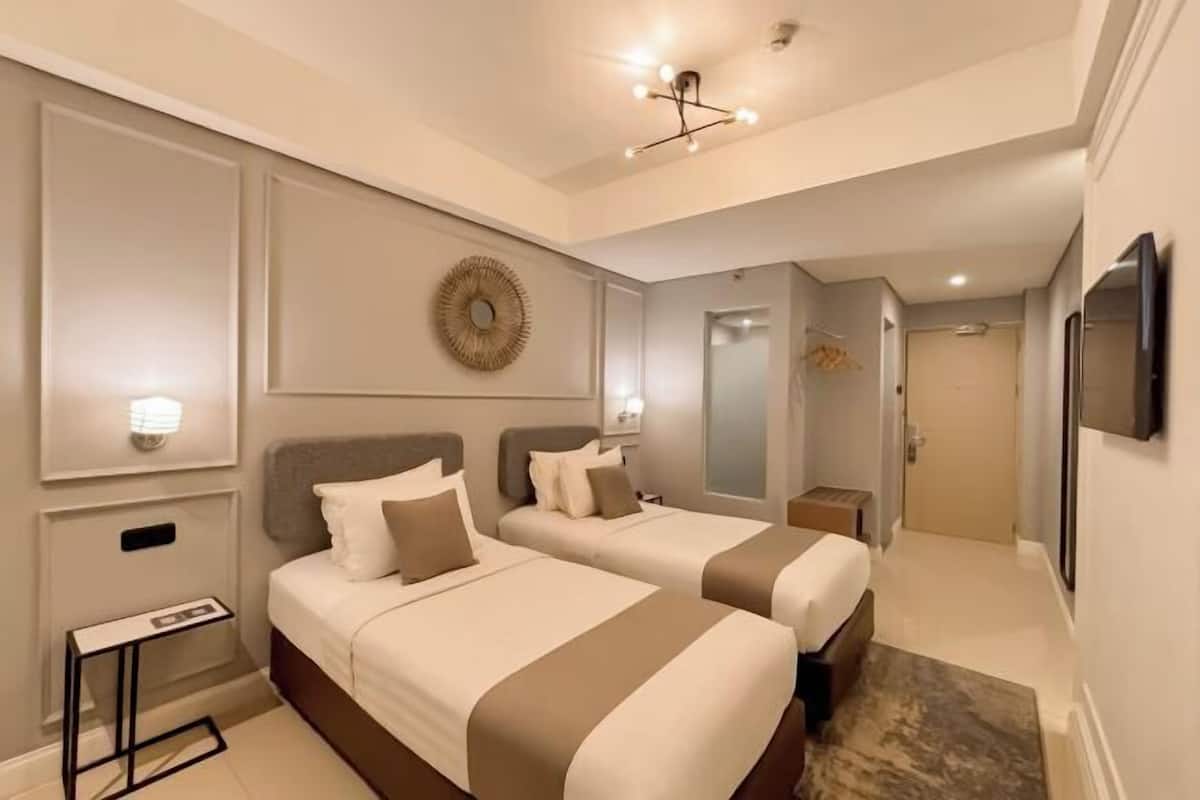 A hotel room with two beds, a flat-screen TV, a bedside table, and a mirror.