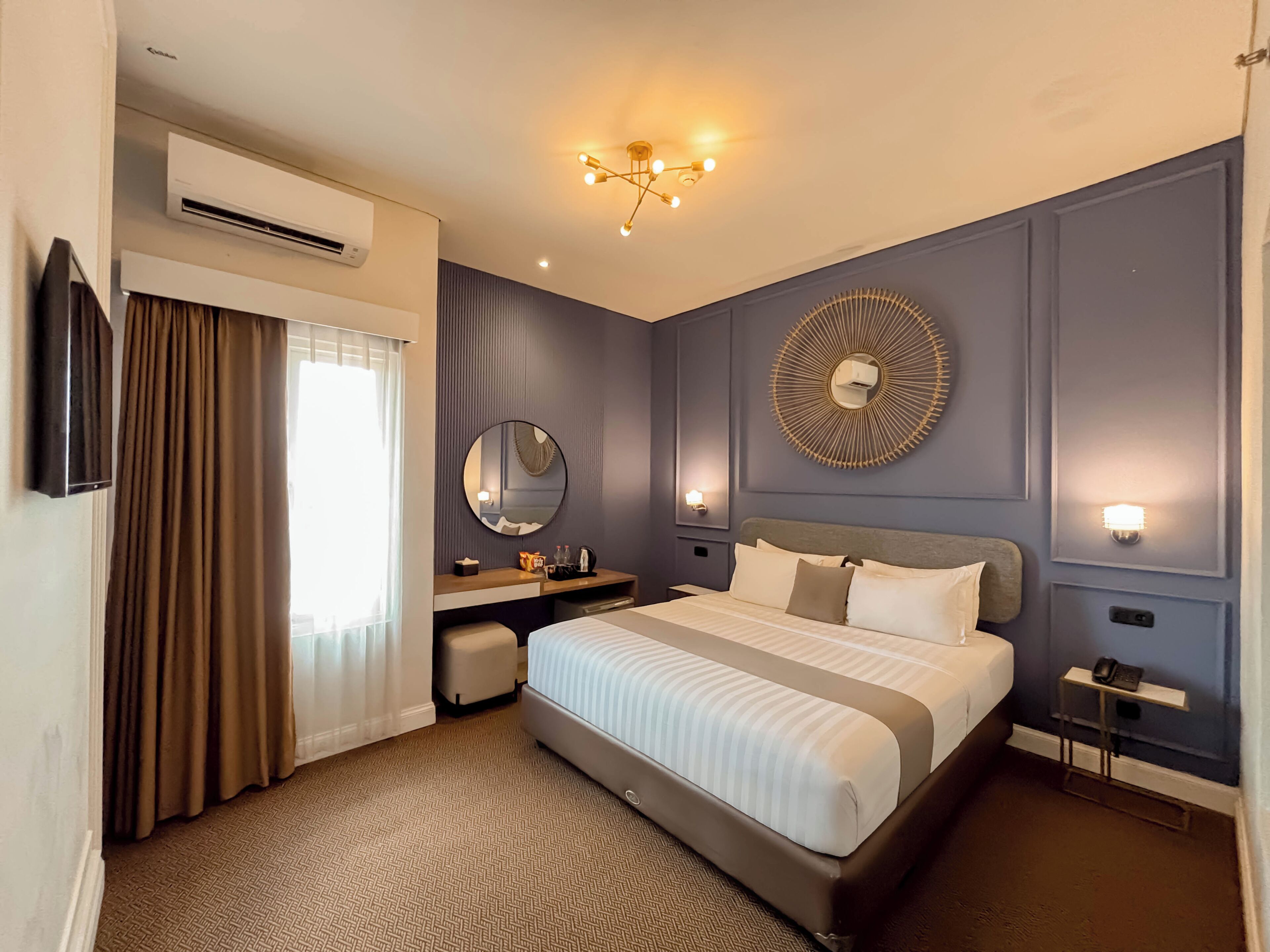 Ein modernes Hotelzimmer mit einem großen Bett, einem Schreibtisch, einem Sessel, einem runden Spiegel und einer Wandleuchte.