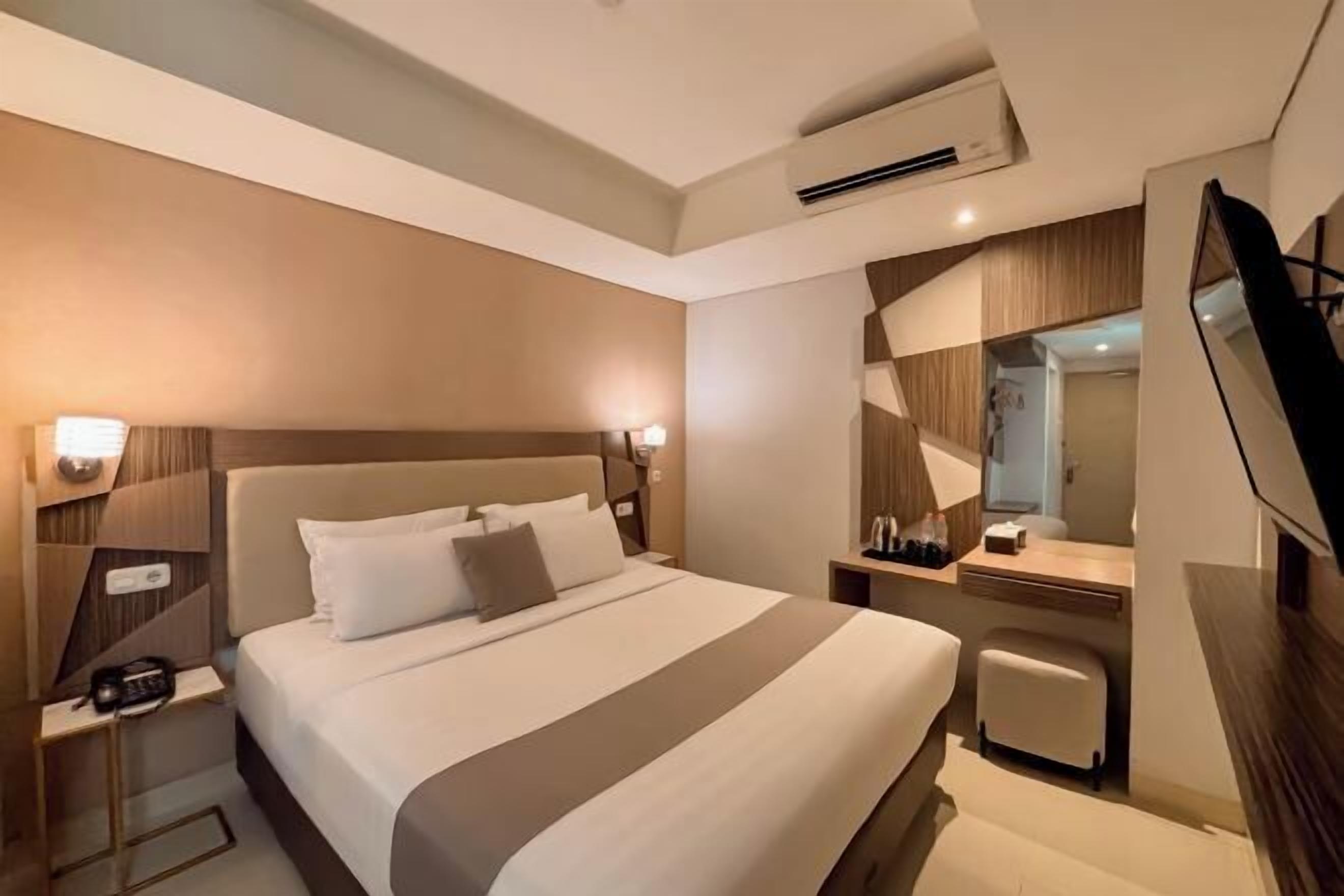 Ein Hotelzimmer mit einem großen Bett, Nachttischen, einem Schreibtisch, einem Sessel, einem Fernseher und einem Spiegel.