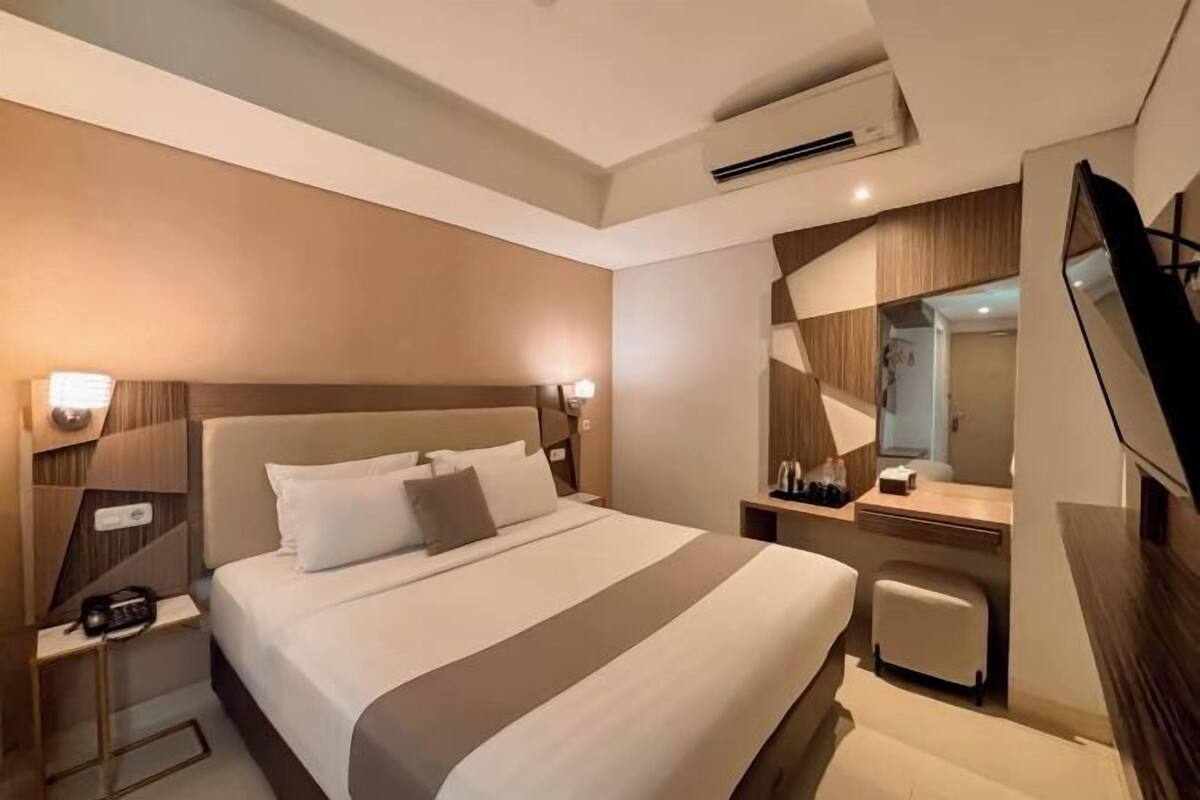 A hotel room with a large bed, bedside tables, a desk, a chair, a TV, and a mirror.