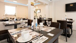 A well-lit dining area with tables set for service, featuring white tableware and silverware. - Bürgerhofhotel Köln (Cologne)