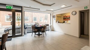 A hotel lobby with a reception desk, a clock, and a view of the street outside. - Bürgerhofhotel Köln (Cologne)