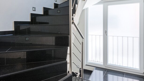 A staircase with black steps and a metal railing leading to a balcony with a white door. - Bürgerhofhotel Köln (Cologne)
