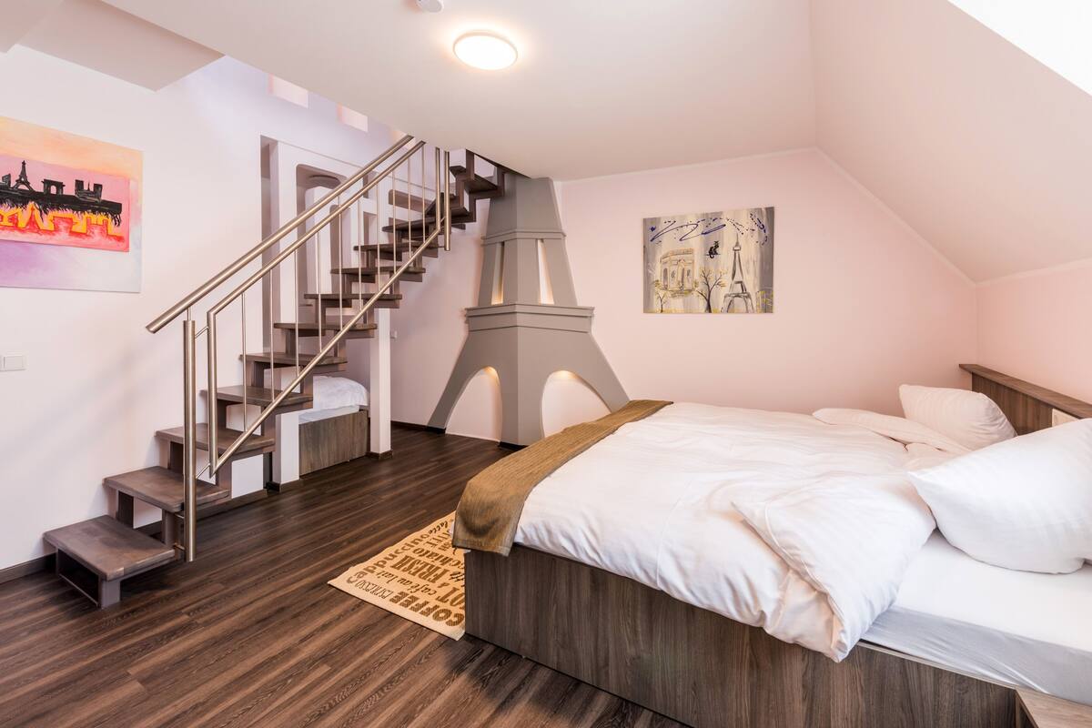 A bedroom with a bed, a wooden floor, a staircase, and a painting of the Eiffel Tower.