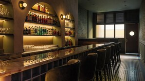 A bar area with multiple shelves of bottles, glasses, and a long counter with bar stools. - Hotel NuVe Heritage (Singapore)