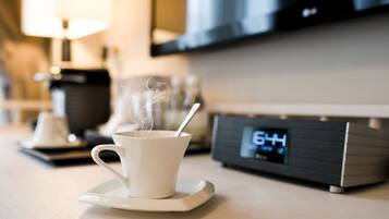 A cup of coffee on a saucer with steam rising, a digital clock displaying 6:44, and a modern kitchen setting in the background.