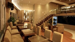 Un moderno vestíbulo de hotel con una amplia zona de estar, una escalera y un gran ventanal.