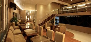 Relax in our spacious lobby, featuring a seating area with tables and chairs, and a staircase leading to an upper level.