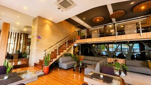 A modern hotel lobby with a staircase, seating area, and a view of the outside. - Hotel Vio Pasteur (Bandung)