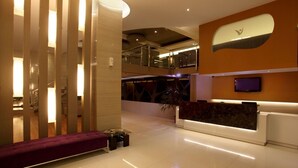 Un moderno vestíbulo de hotel con mostrador de recepción, zona de estar y una escalera que lleva a un nivel superior.