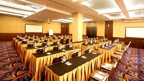 Un salón de conferencias con varias mesas, sillas y una pantalla para proyector.