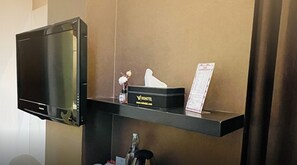 A hotel room with a flat-screen TV mounted on the wall, a minibar with a bottle and a glass, and a sign for VIO Hotel Pasteur. - Hotel Vio Pasteur (Bandung)
