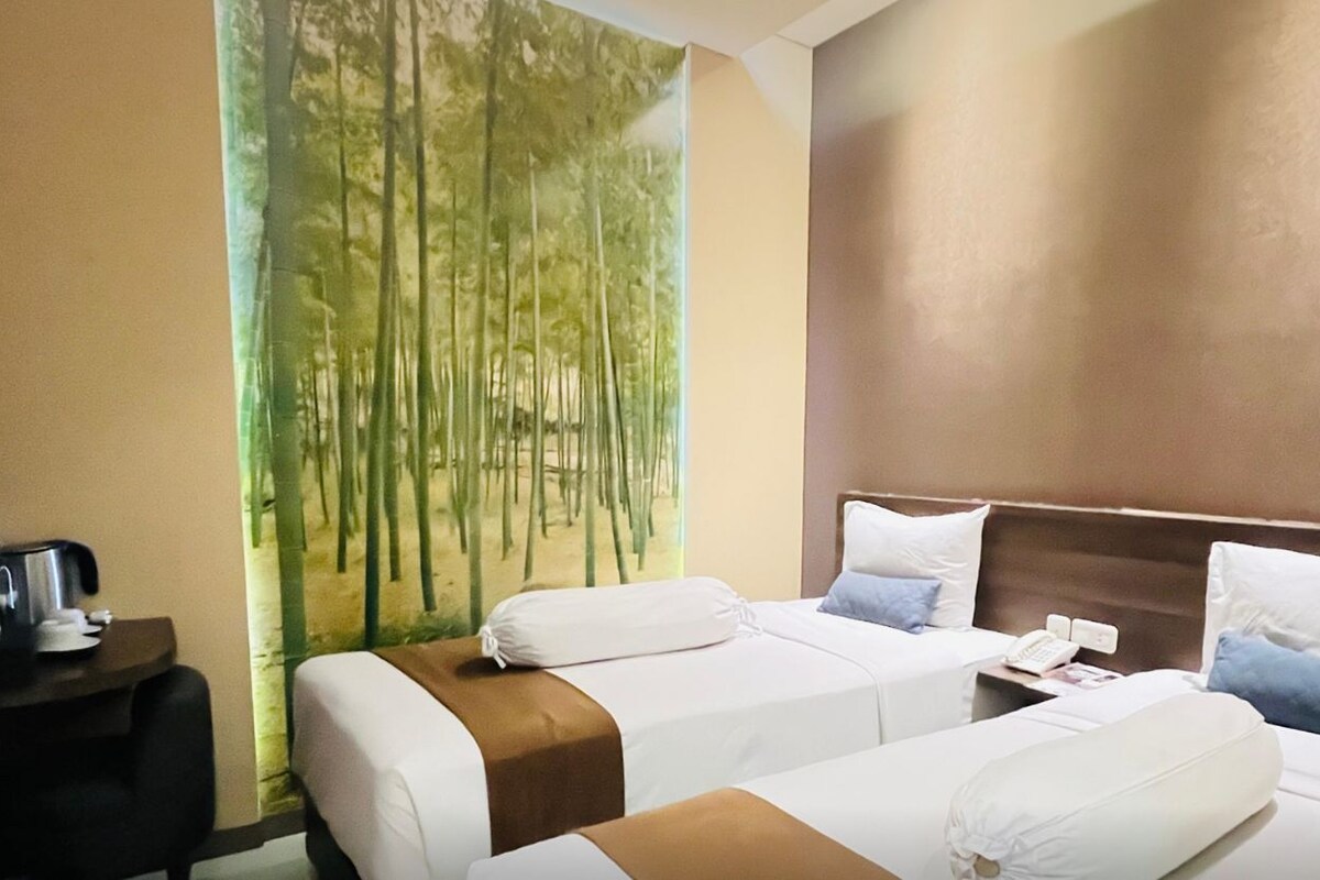 A hotel room with two beds, a nightstand, and a painting of bamboo.
