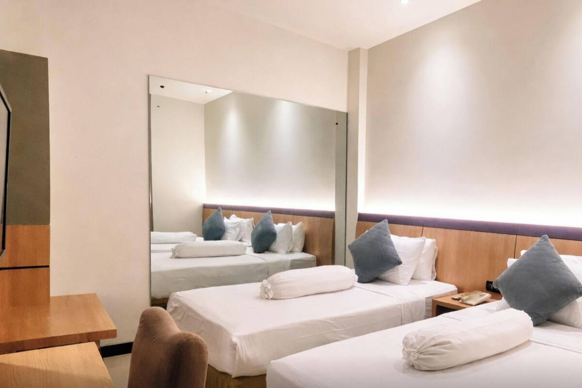 Une chambre d’hôtel avec deux lits simples, une tête de lit en bois, un miroir et une table de chevet en bois.
