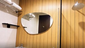 Ein Badezimmer mit einer Holzwand, einem runden Spiegel, einem Handtuchhalter, einer Duschbrause und einer kleinen Ablagefläche.