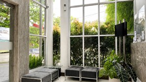 A modern interior with large windows, a flat-screen TV, and a seating area with cushioned benches. - Hotel Vio Express Surapati Bandung (Bandung)