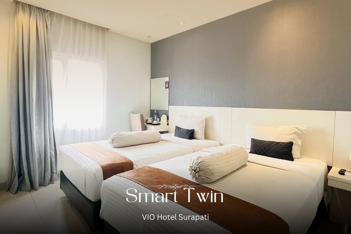 A hotel room with two beds, a large mirror, and a window with curtains.