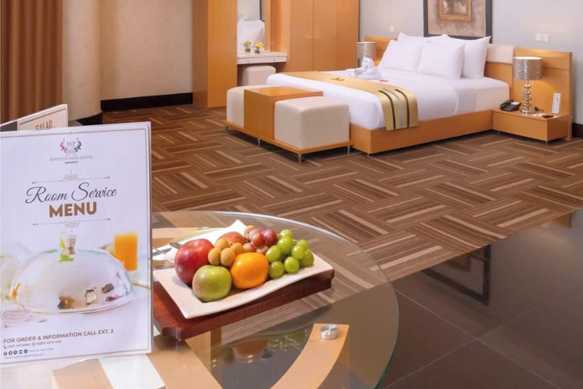 A hotel room with a bed, bedside tables, a glass coffee table with fruit, and a room service menu sign.