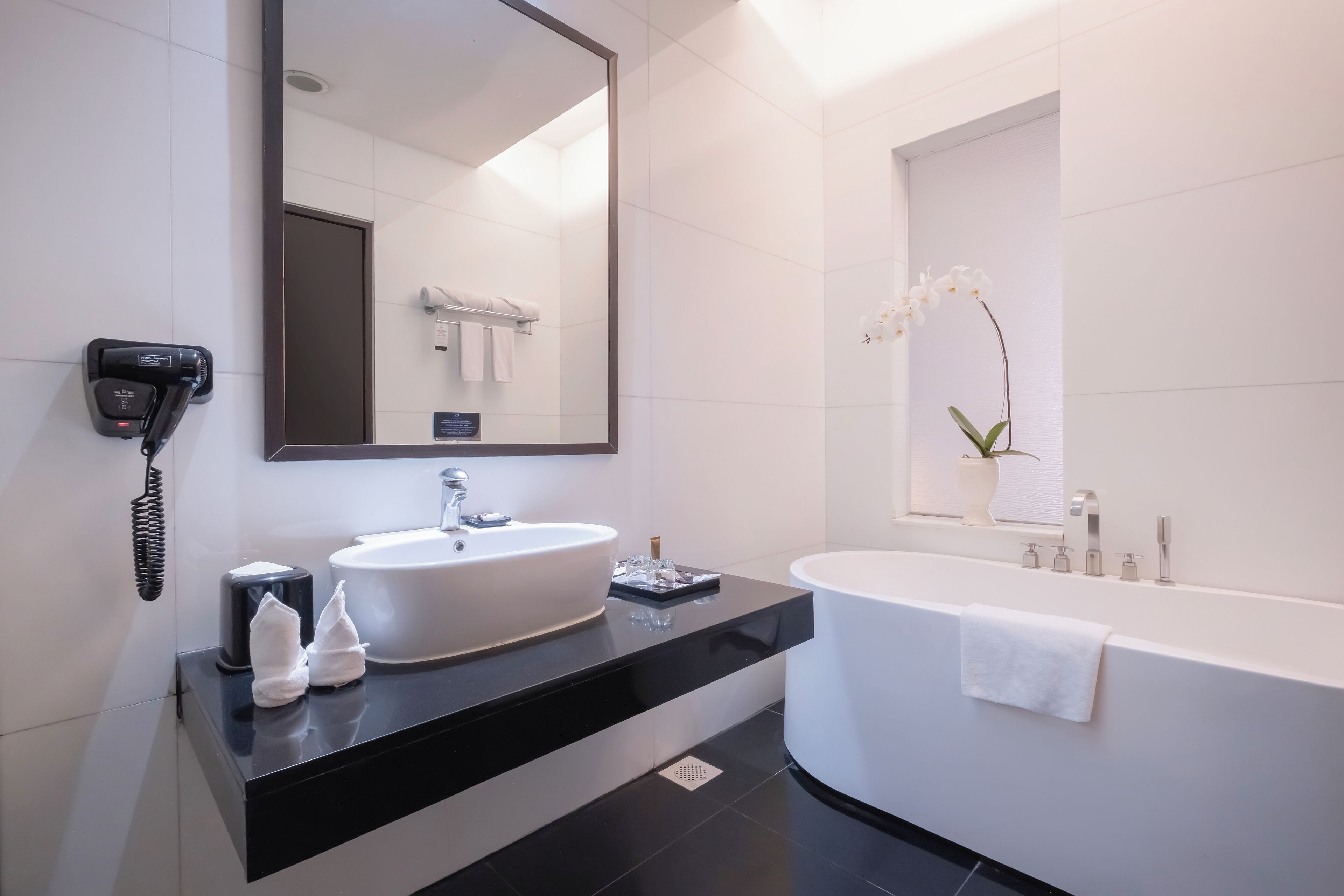 A modern bathroom with a large mirror, a sink, a bathtub, and a potted orchid.