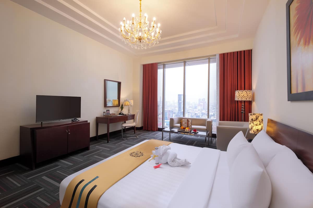 A hotel room with a large bed, a television, a desk, and a view of the city.