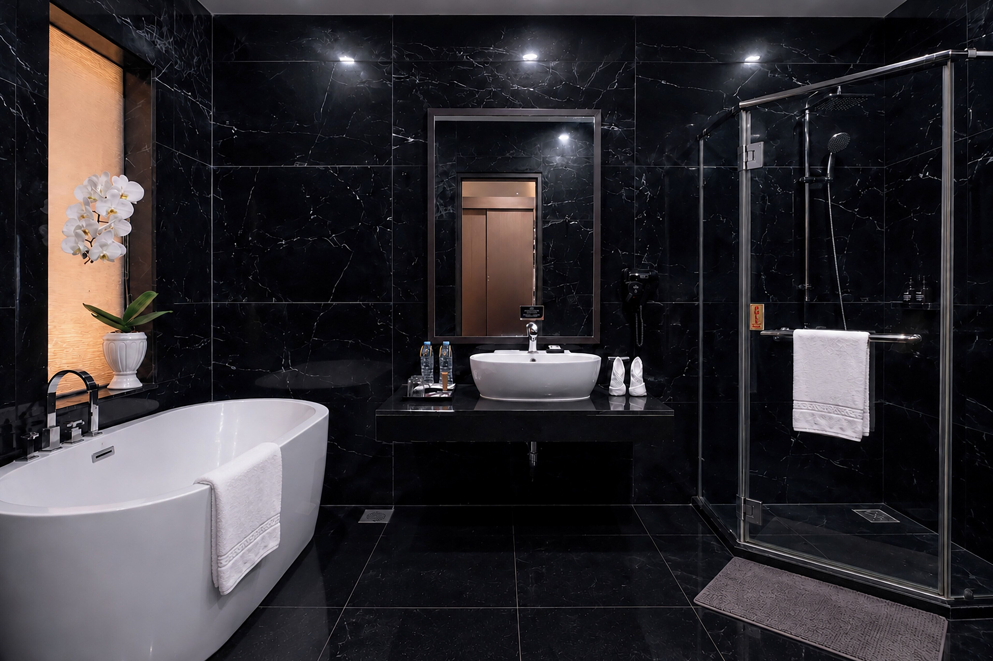 Een moderne badkamer met een vrijstaand bad, een grote spiegel, een douche met glazen wanden en een betegelde muur van marmer.