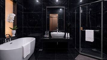 Een moderne badkamer met een vrijstaand bad, een grote spiegel, een douche met glazen wanden en een betegelde muur van marmer.