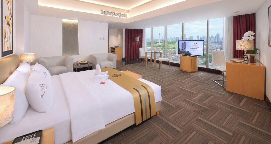 A hotel room with a large bed, a desk, a TV, and a city view.