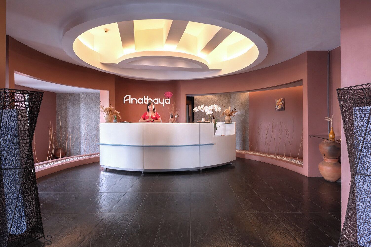 A reception area with a curved reception desk, a wall-mounted sign reading 'Anathaya,' and a modern ceiling design.