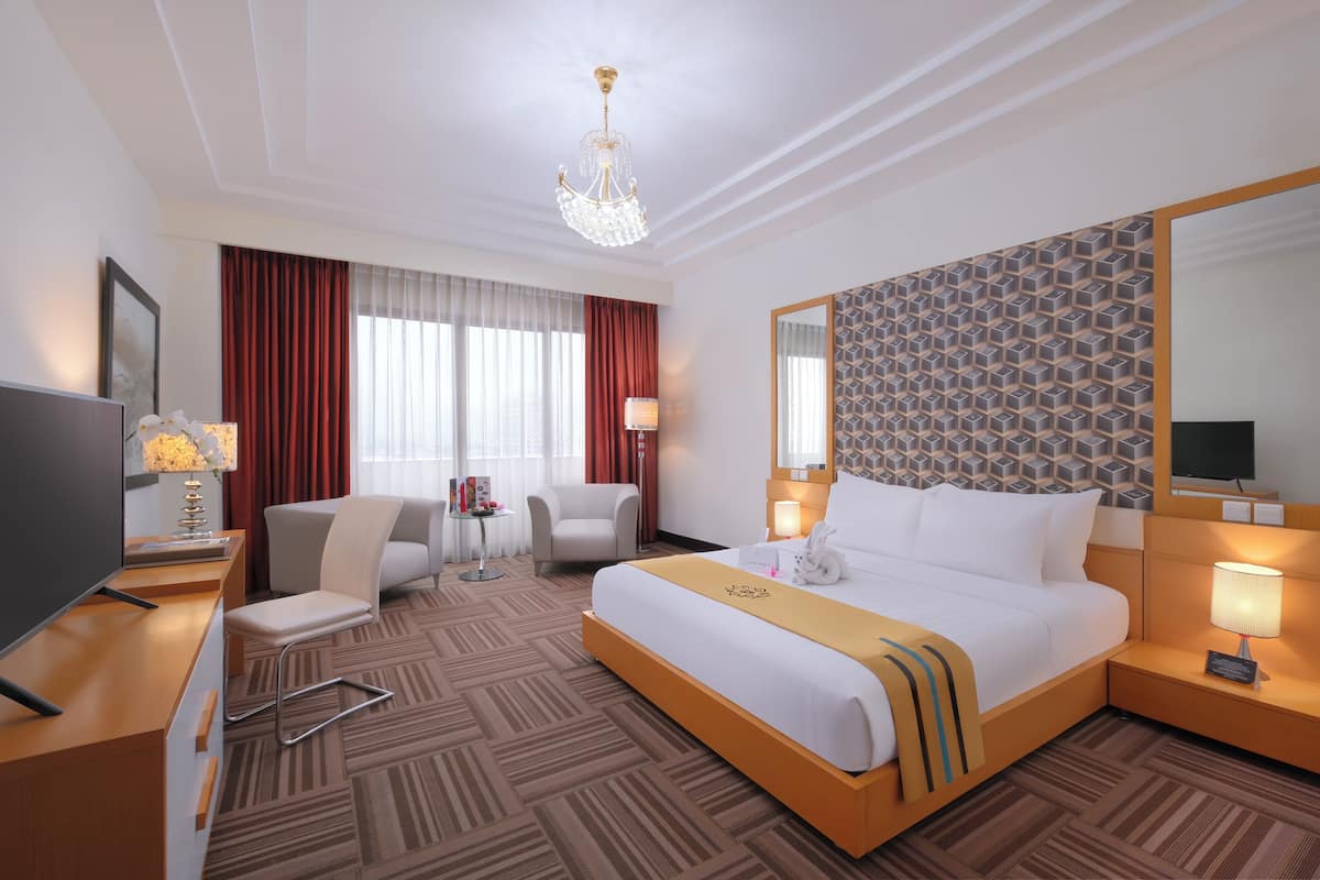 A hotel room with a large bed, a desk, a chair, a TV, and a chandelier.