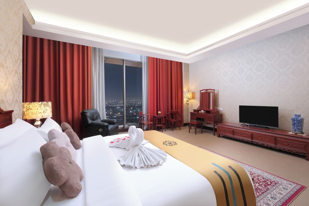 A hotel room with a large bed, a flat-screen TV, a desk, and a view of the city at night.