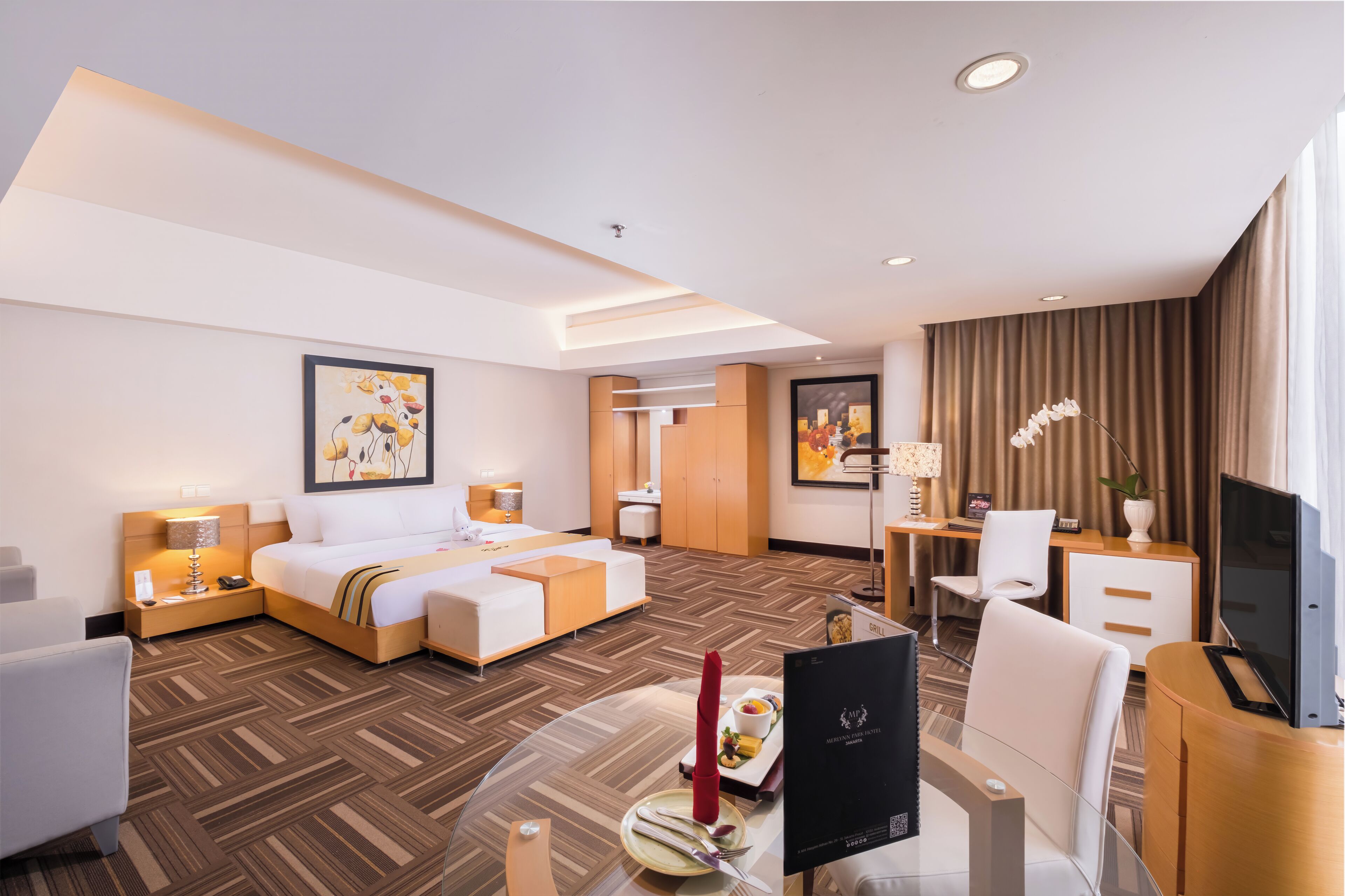 Quarto de hotel com cama, escrivaninha com computador, televisão e área de jantar com mesa e cadeiras.