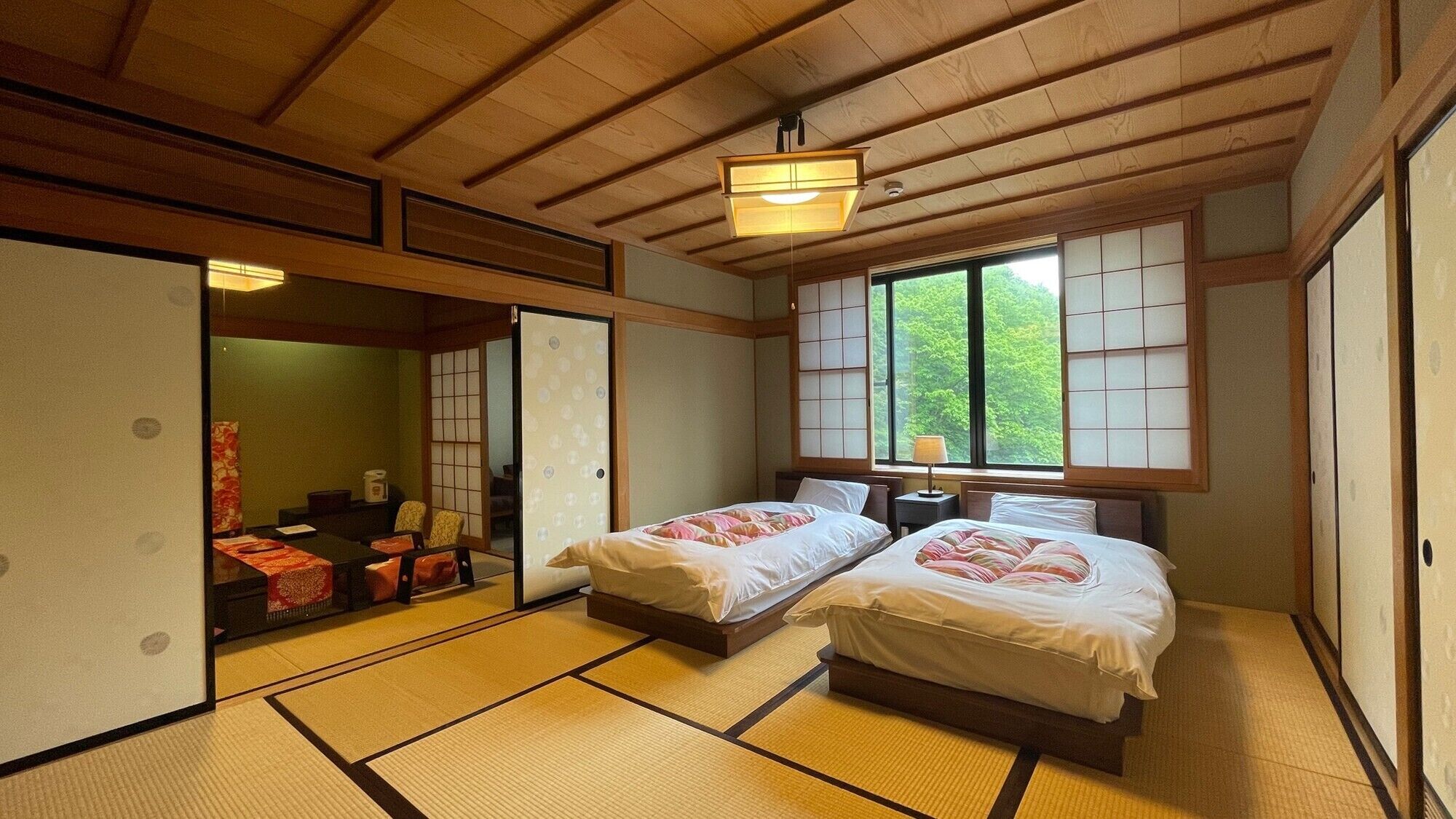 Een traditionele Japanse kamer met tatami vloeren, twee bedden, een schuifdeur en uitzicht op groen buiten.